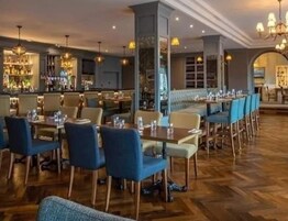 Un restaurante con suelo de madera, sillas azules y beige, y una zona de bar con mostrador.