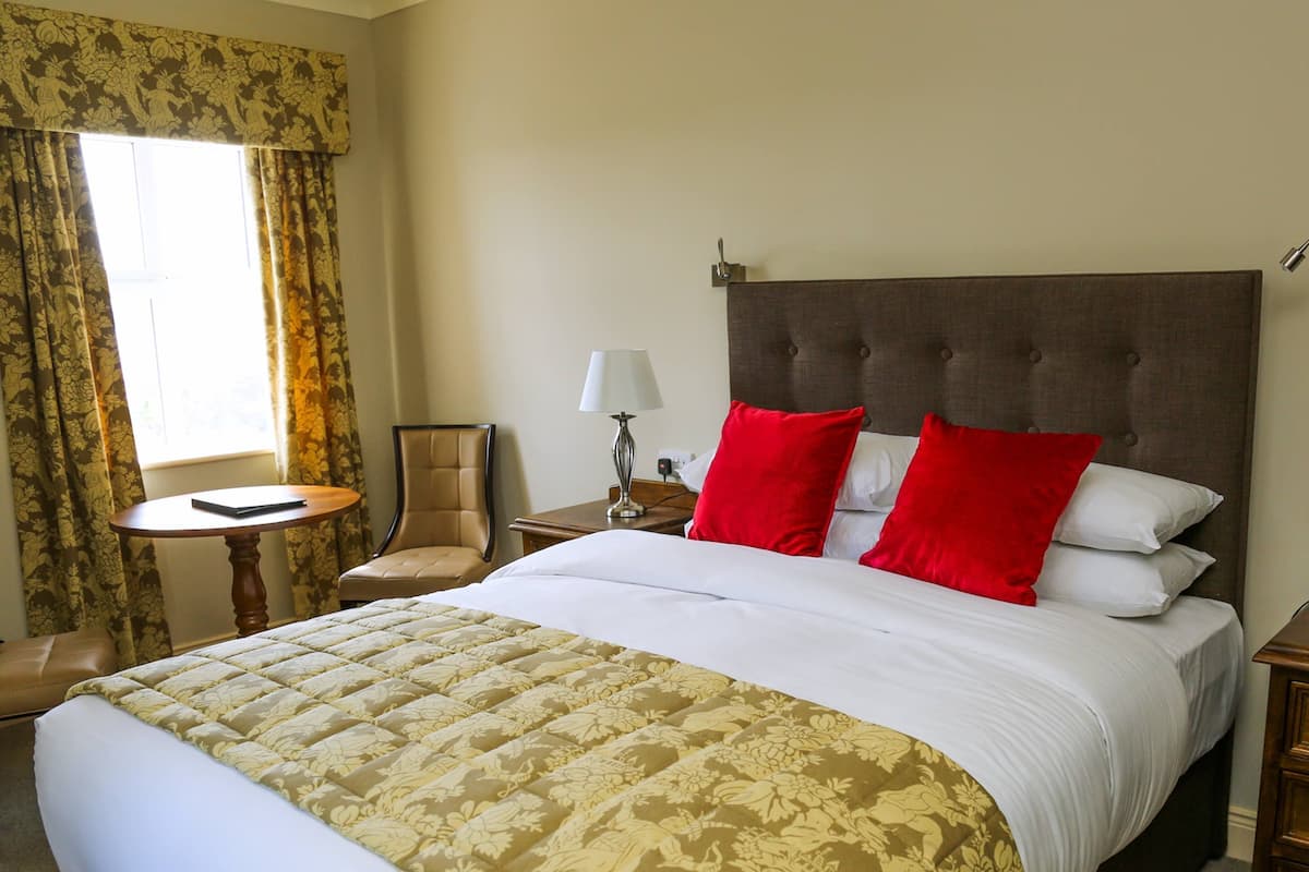 A hotel room with a large bed, a chair, a small table, and a lamp.