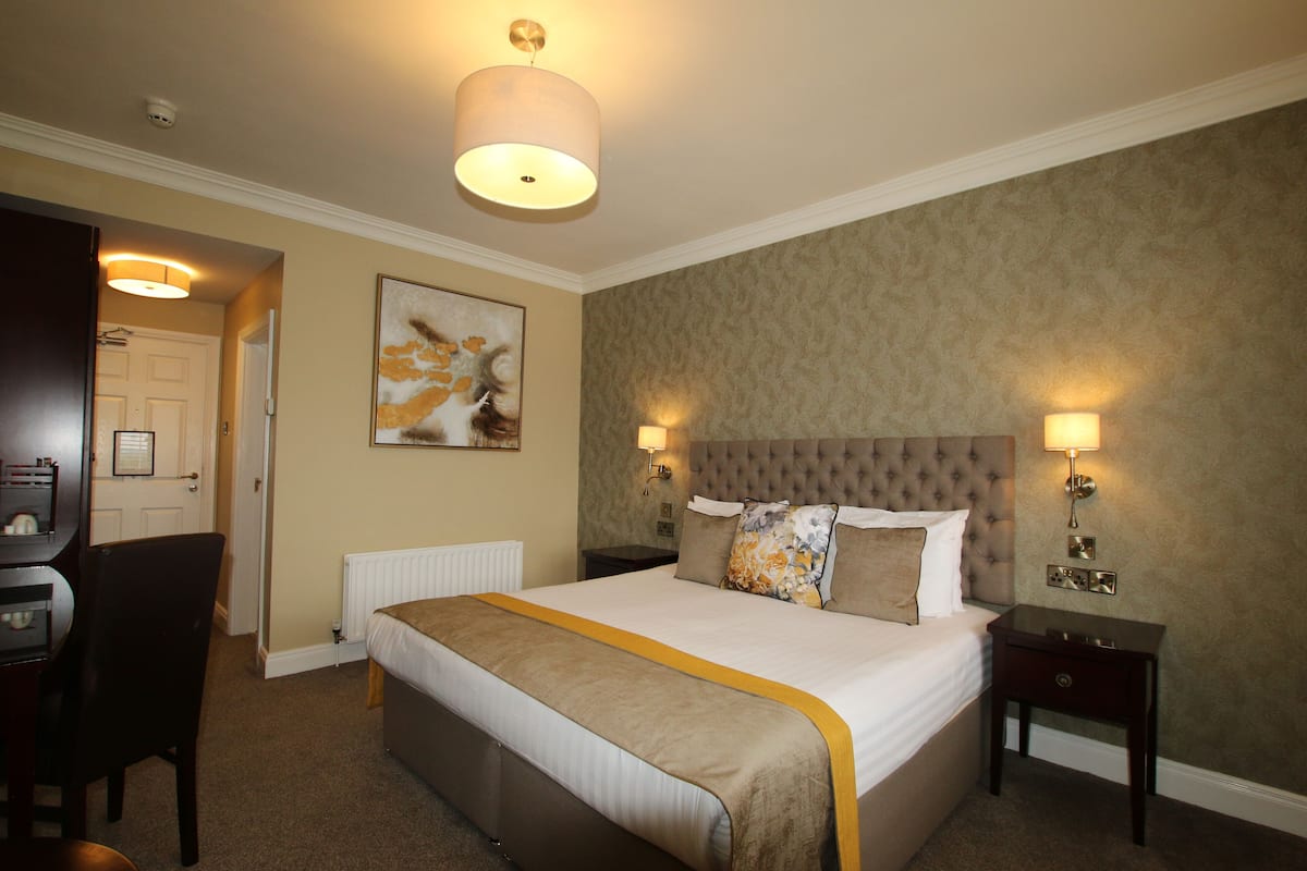 A hotel room with a large bed, two bedside tables, a chair, a desk, and a radiator.