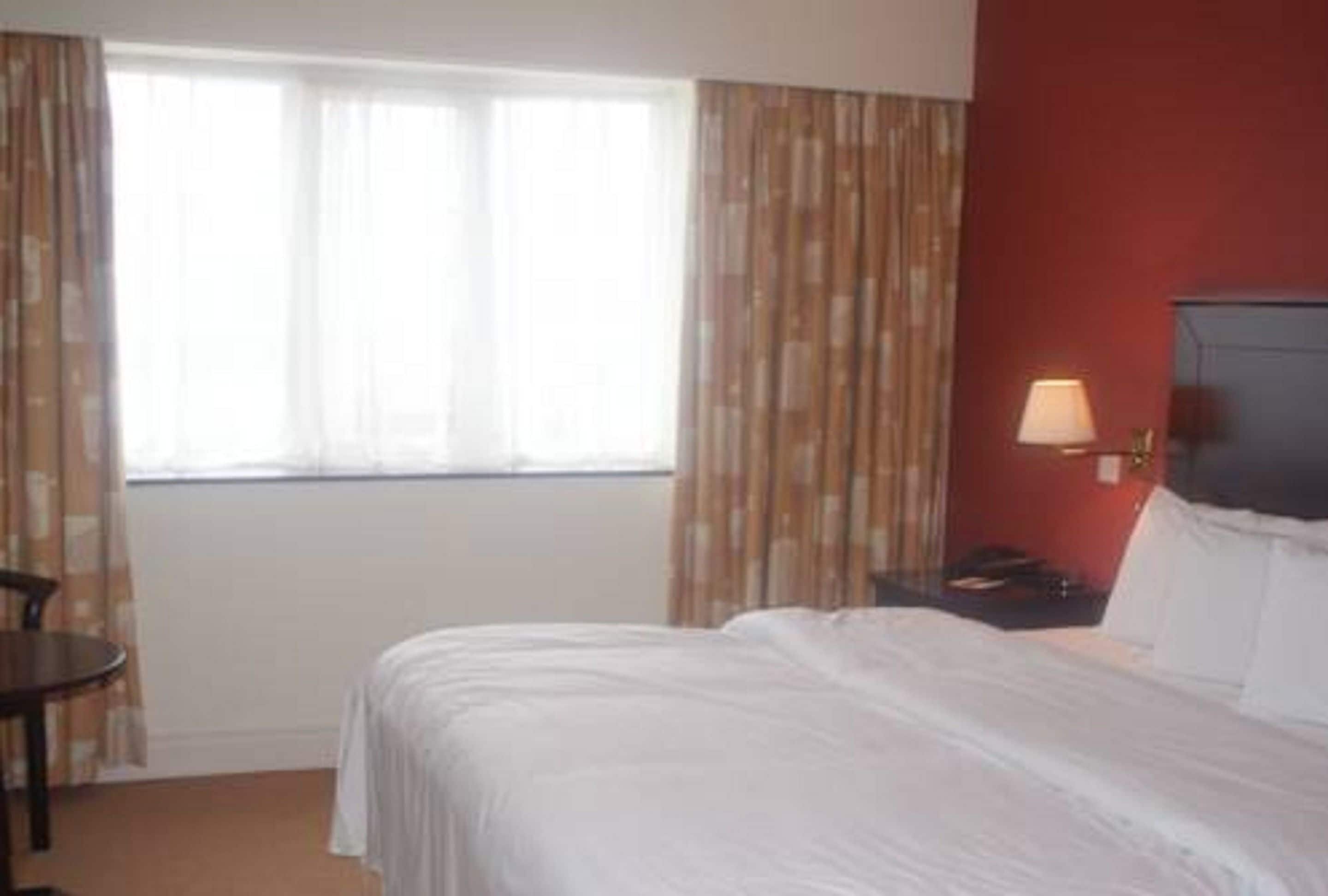 A hotel room with a bed, a nightstand, a lamp, a chair, and a window with curtains.