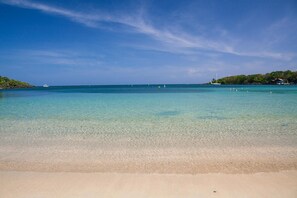 Una playa con agua turquesa cristalina, una orilla arenosa y un pequeño bote a lo lejos.