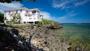 A beachfront property with a multi-story building, clear ocean water, and rocky shoreline.