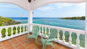 A balcony with two green chairs, white balustrades, and a view of the ocean.