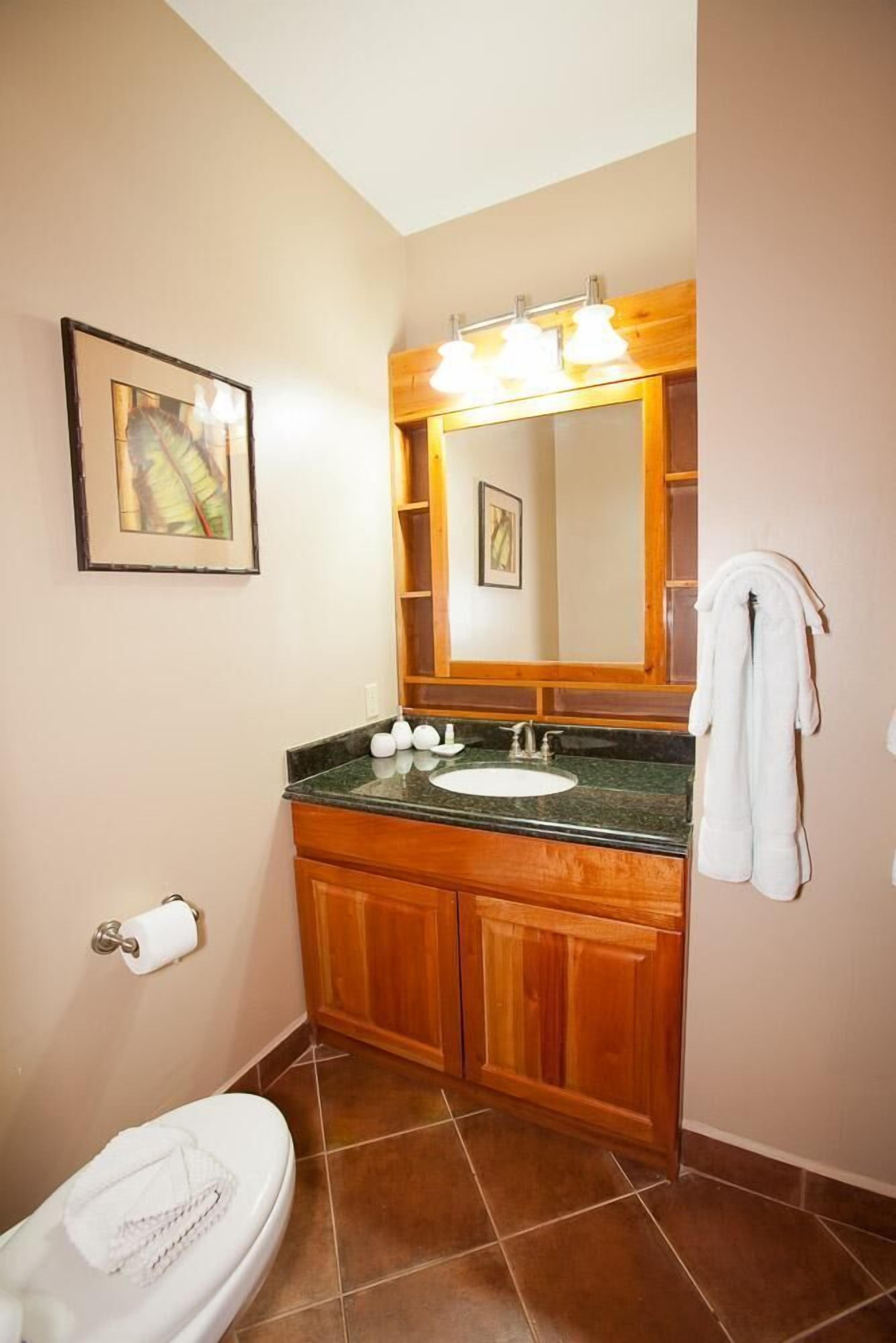 A bathroom with a wooden vanity, a sink, a mirror, and a toilet.