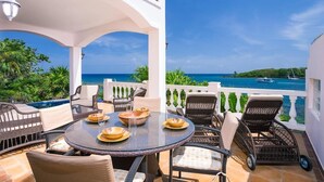 A covered outdoor seating area with a view of the sea, featuring wicker furniture and a round table with plates and bowls. - Coral Vista 3 2 bedroom option (Roatan)