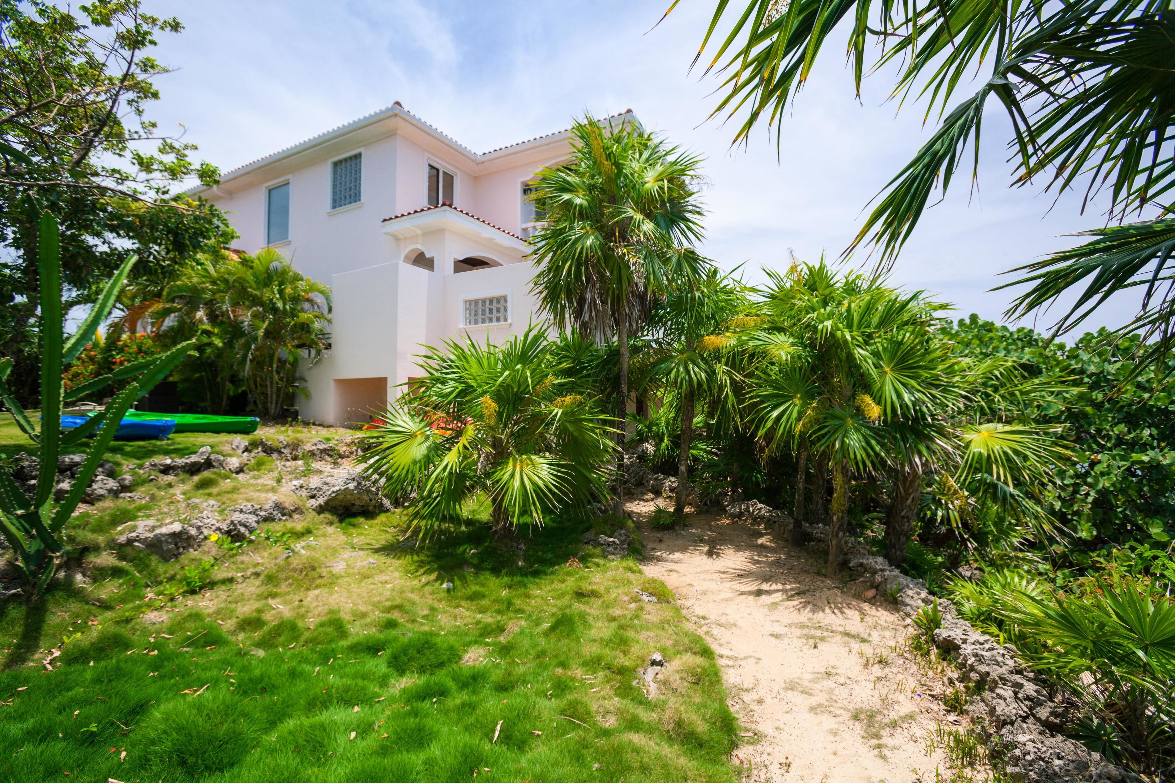 A house with a garden path leading to a white building with a pink facade.