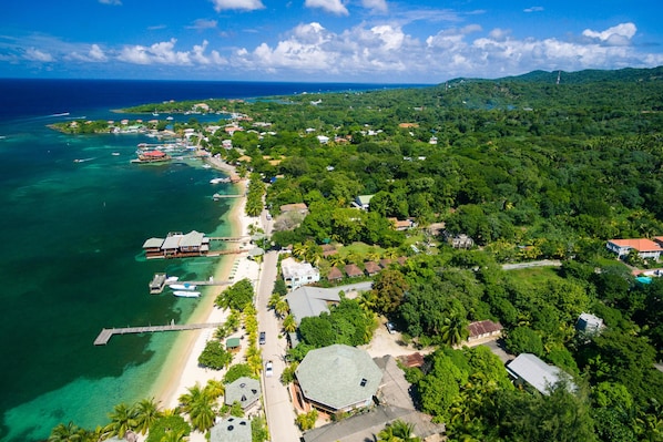 An aerial view of a coastal area with a beach, clear waters, and a mix of residential and commercial buildings.