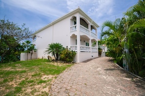 A two-story building with a white exterior, a balcony on the second floor, and a paved pathway leading to the entrance.