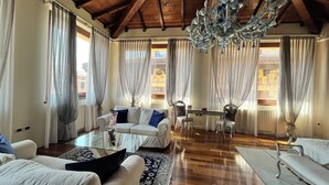 A spacious living room with a wooden ceiling, a glass coffee table, a sofa, a dining table with chairs, and a chandelier. - Relais A Ponte Pietra (Verona)