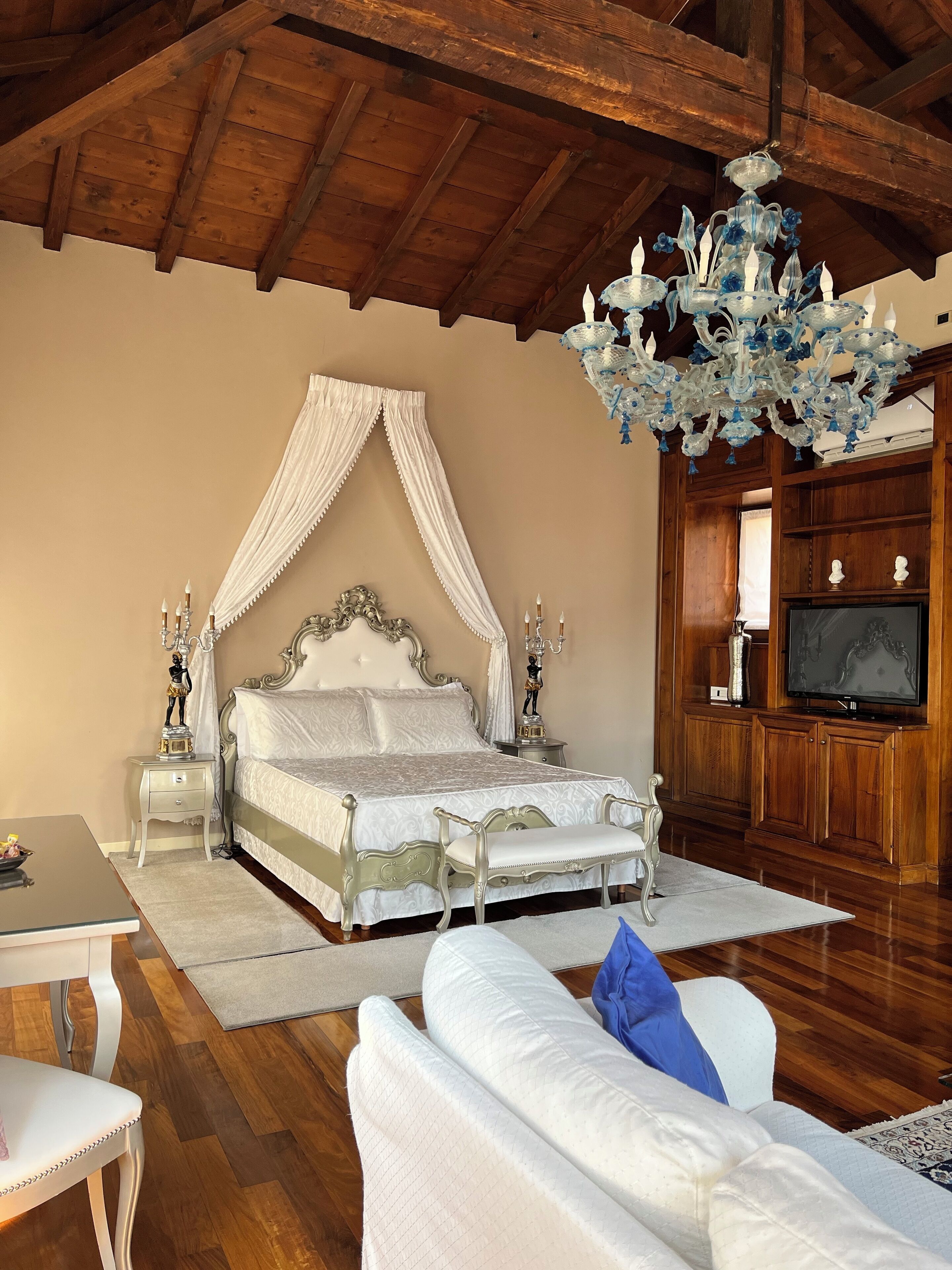 A bedroom with a four-poster bed, a chandelier, a television, and wooden paneling.