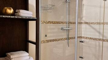 A glass-enclosed shower with a handheld showerhead, a towel rack, and a shelf with towels and a decorative bowl.