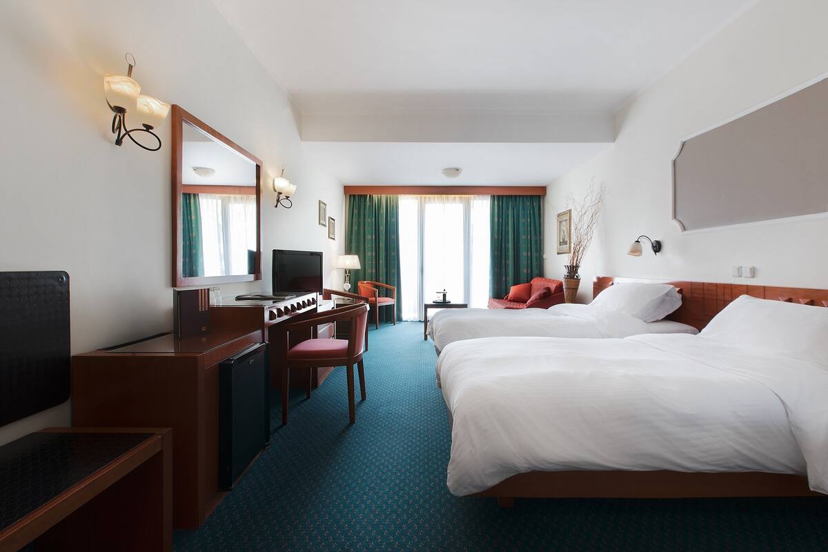 Ein Hotelzimmer mit zwei Betten, einem Schreibtisch mit Computer, einem Fernseher und einem großen Spiegel.