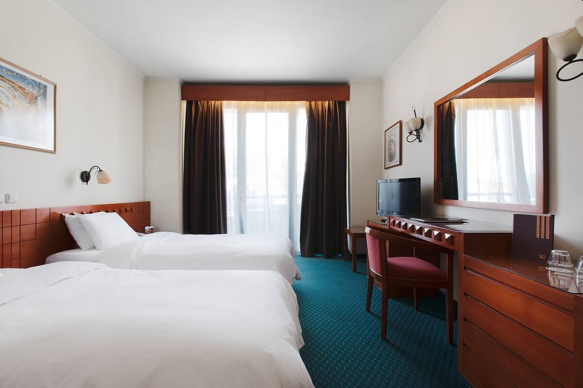 Ein Hotelzimmer mit zwei Betten, einem Schreibtisch mit Stuhl, einem Fernseher und einem großen Spiegel.
