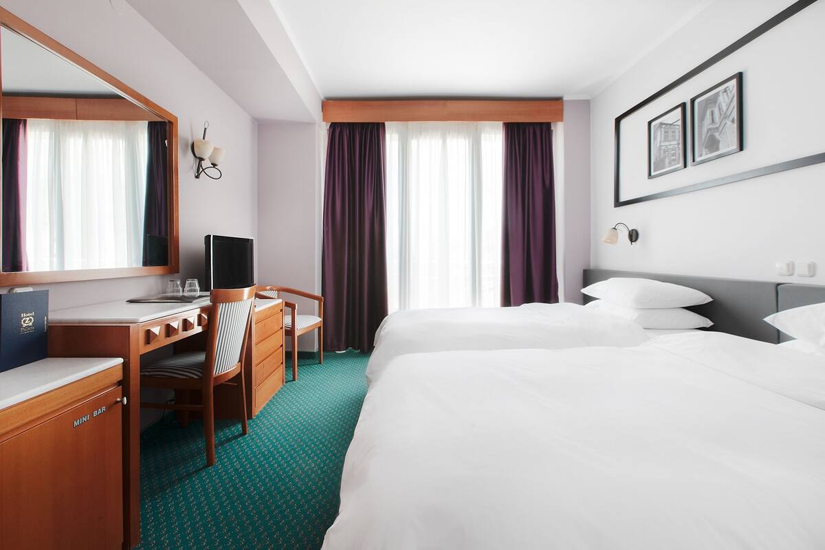Ein Hotelzimmer mit einem Bett, einem Schreibtisch mit Computer, einem Sessel, einer Minibar und einem großen Spiegel.