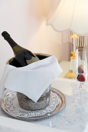 A bottle of champagne in a decorative bowl with a white napkin, a glass with a strawberry, and a candle holder in the background. - Hotel Z Palace & Congress Center (Xanthi)