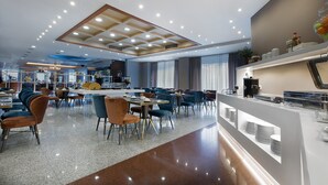 Un comedor moderno con varias mesas y sillas, una zona de bar central, y un techo bien iluminado con luces empotradas.