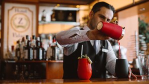Un cantinero sirviendo una bebida en una taza negra, con una taza roja sobre la barra.
