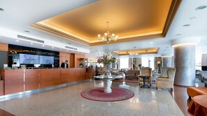 Un vestíbulo de hotel con mostrador de recepción, un candelabro y una mesa central con un jarrón de flores.
