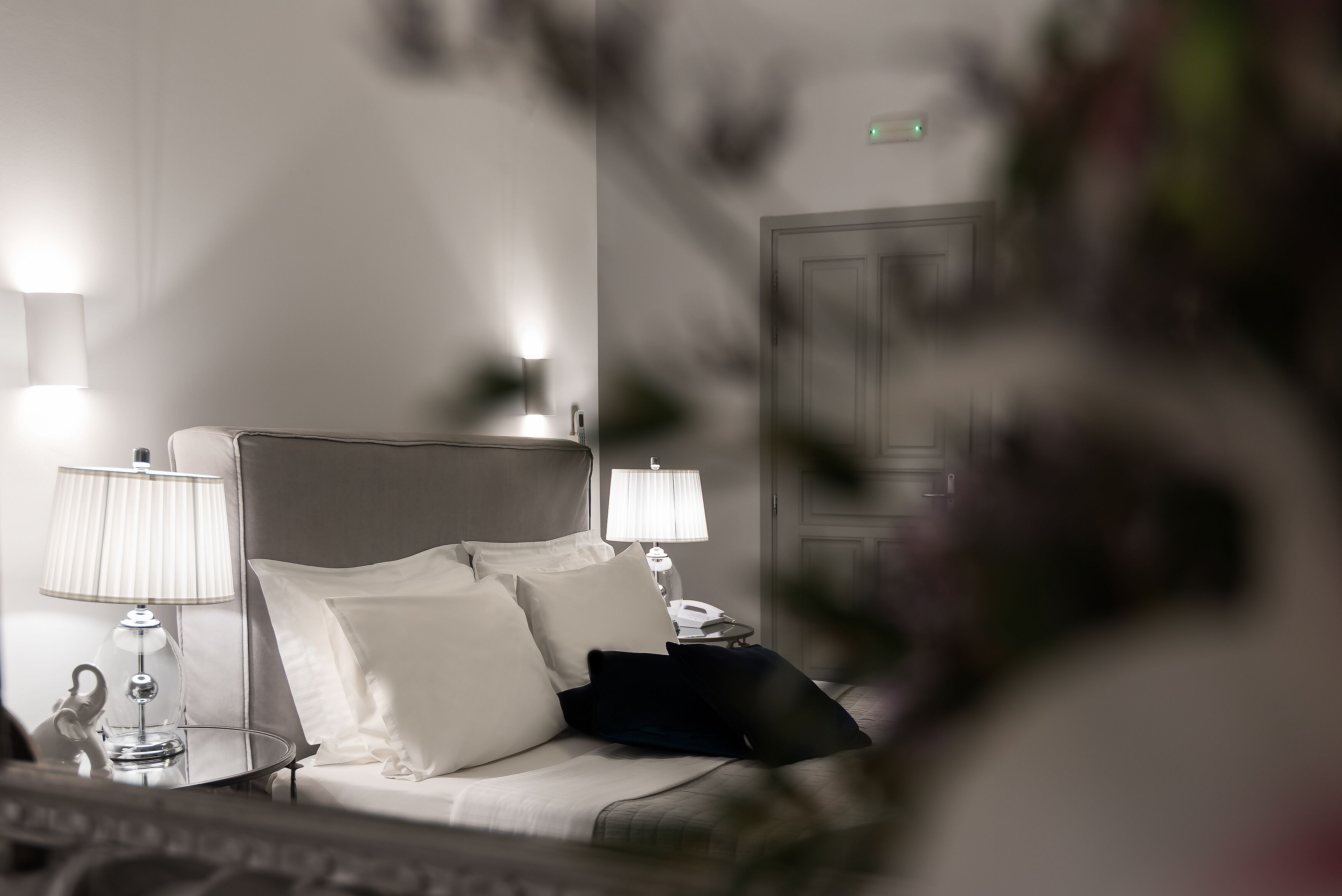 Cama bem arrumada com almofadas brancas e escuras, duas luminárias de cabeceira e uma mesa de cabeceira com telefone.