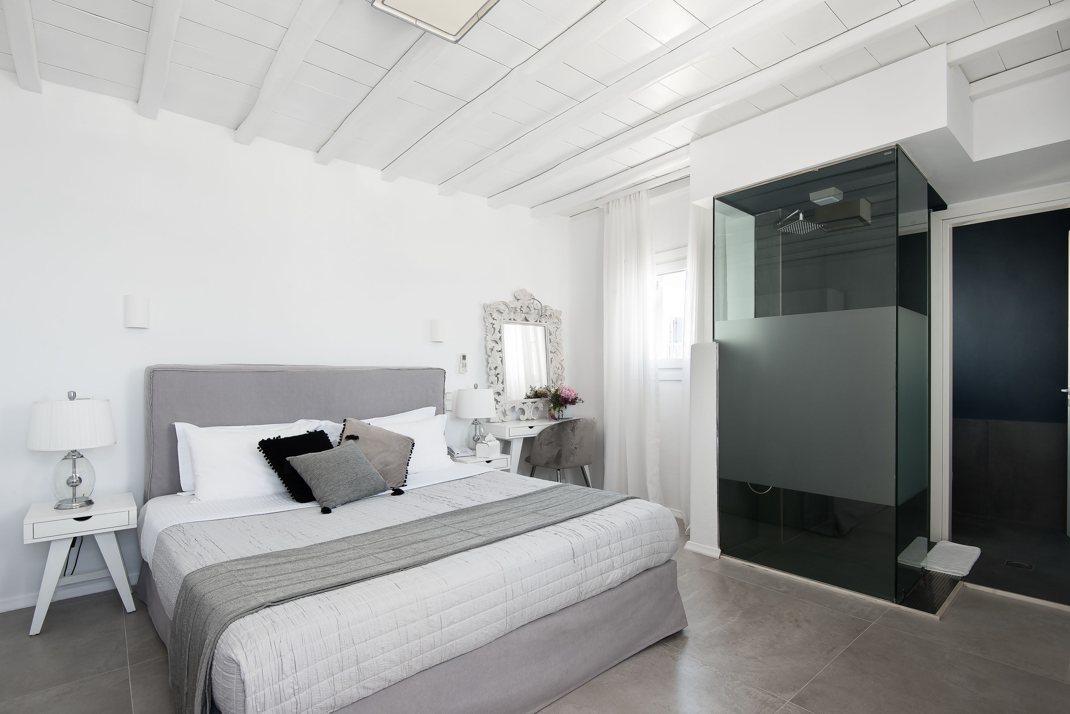 A modern bedroom with a large bed, a nightstand, a desk, and a glass-enclosed shower area.