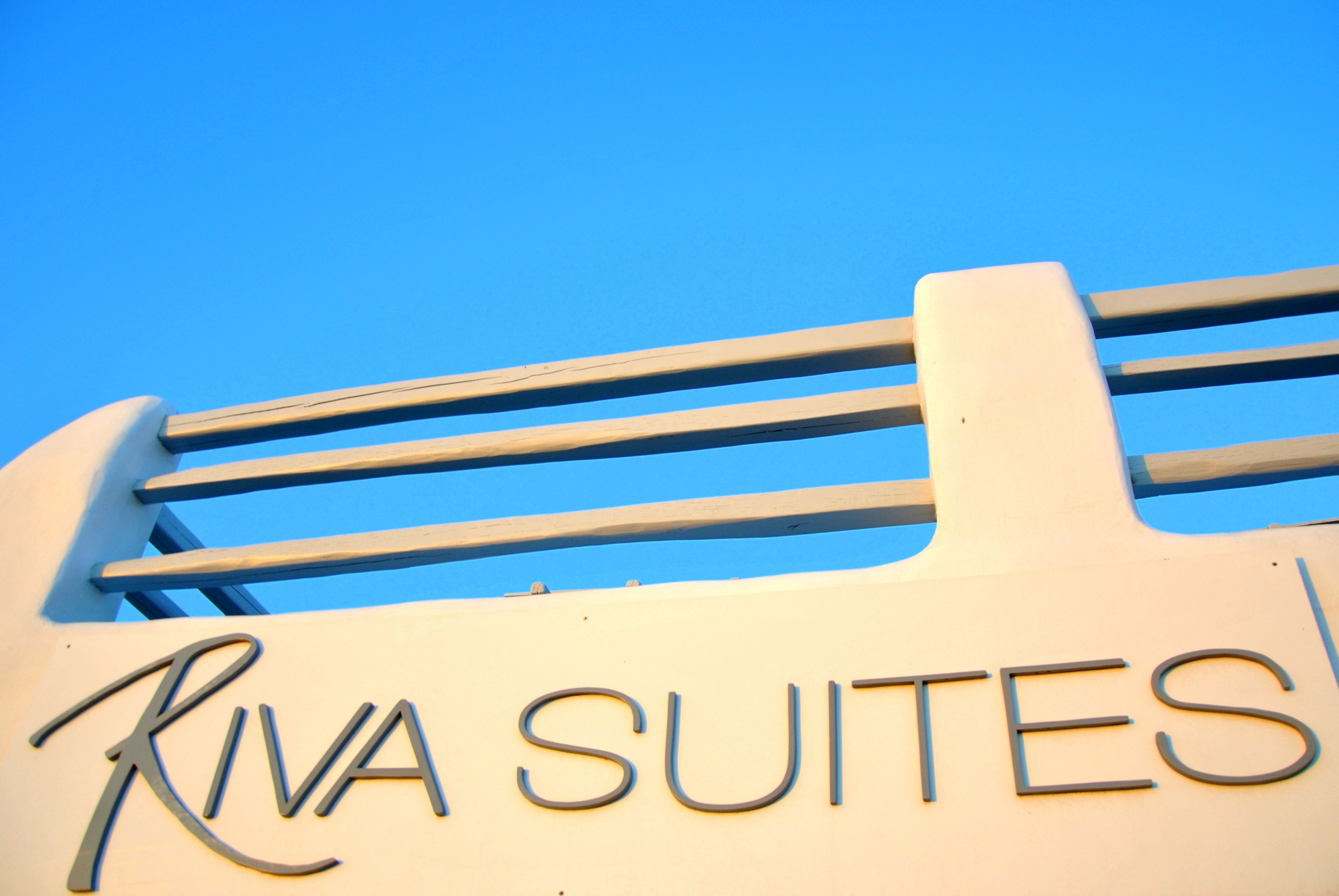 A sign for Riva Suites with a clear blue sky in the background.