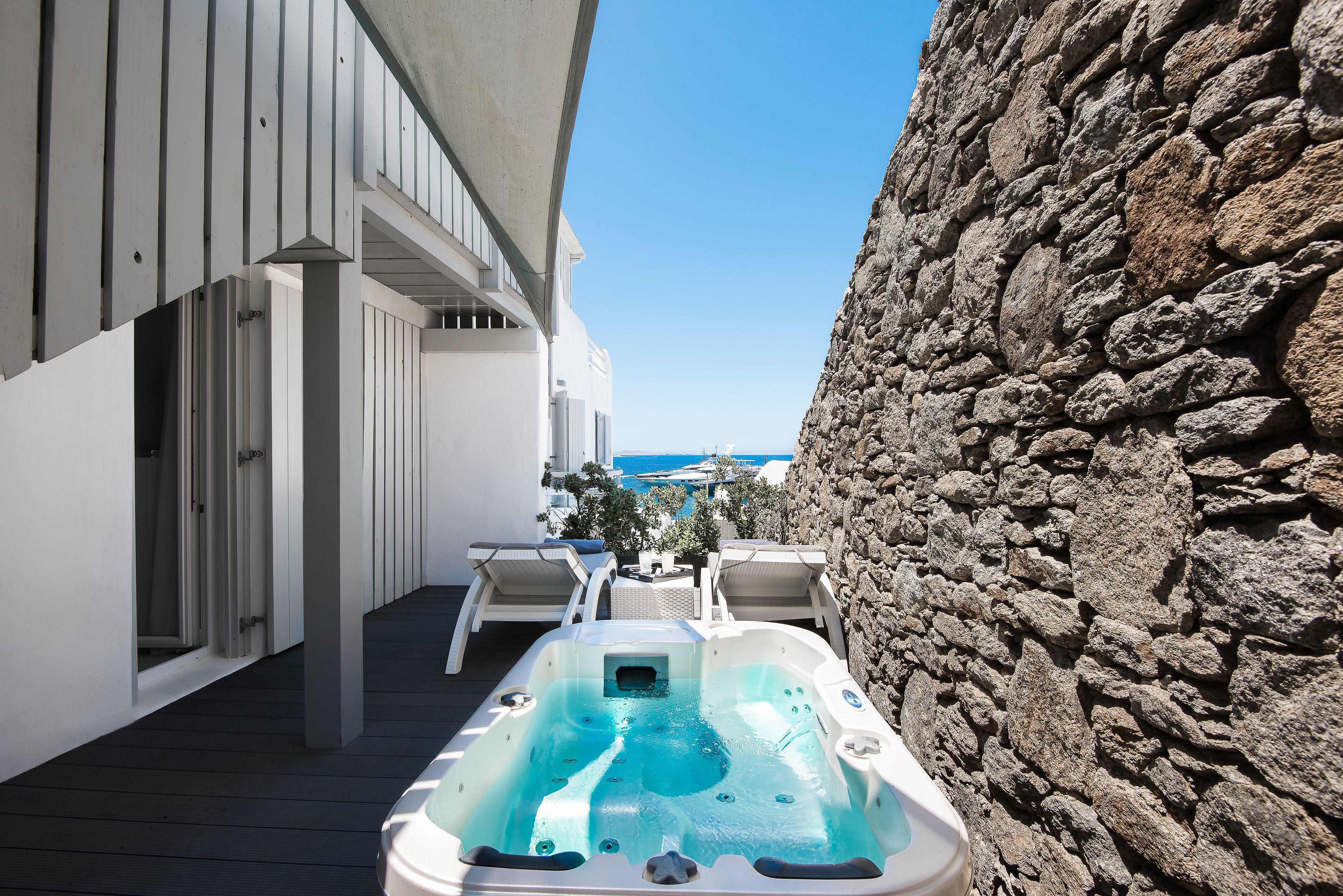 A hot tub on a wooden deck with a stone wall and a view of the sea.