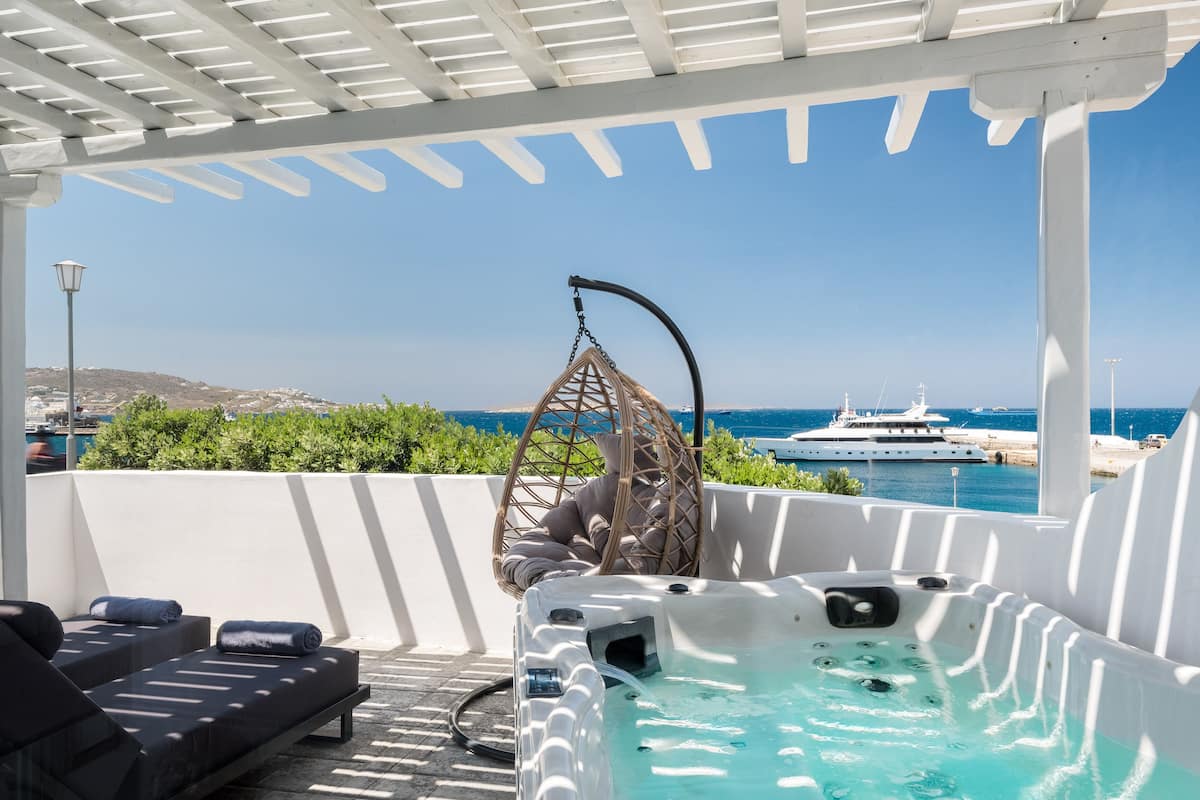 Terraza en la azotea con jacuzzi, sillones de descanso y una silla colgante con vistas a un puerto deportivo y barcos.
