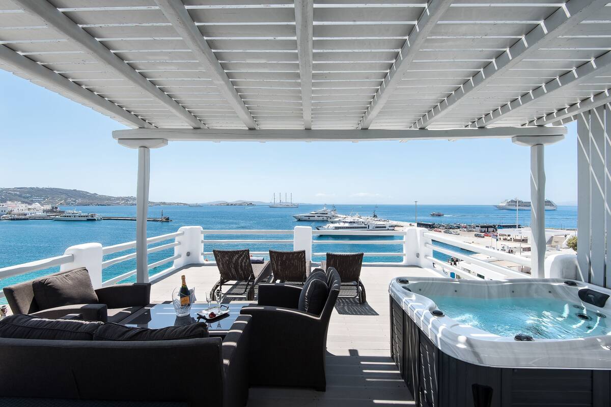 Un área de estar al aire libre techada con jacuzzi, con vista a un puerto deportivo lleno de barcos y yates.