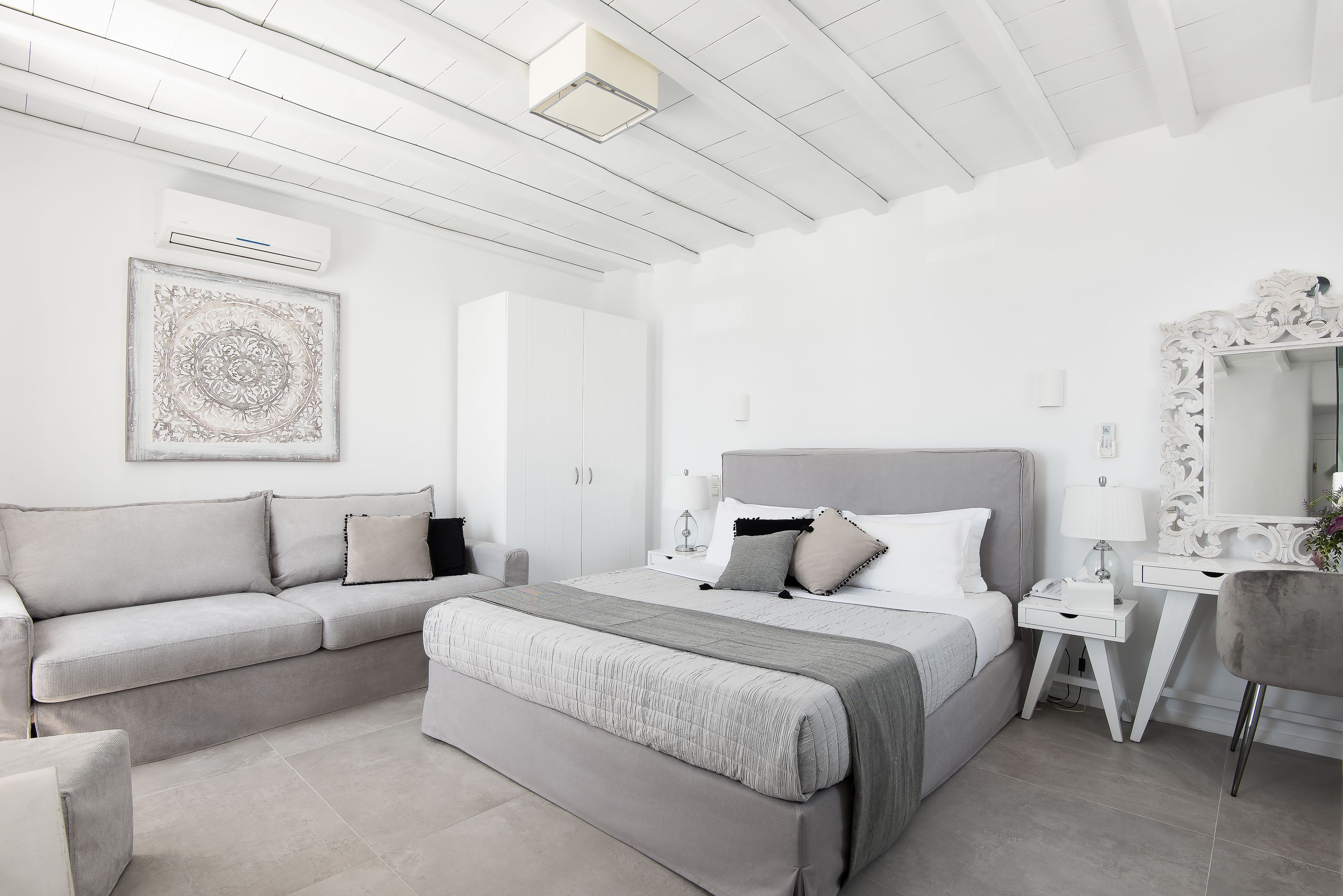 A modern bedroom with a large bed, a sofa, a desk, and a mirror.