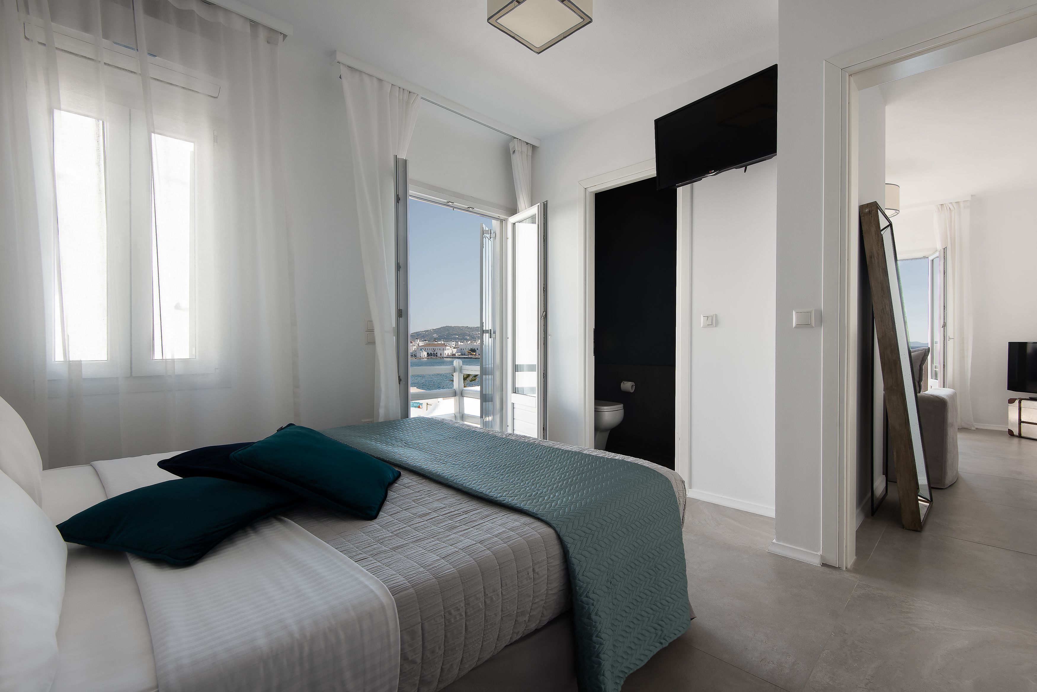 Een slaapkamer met een bed, uitzicht op zee en een deur die naar een andere kamer leidt.