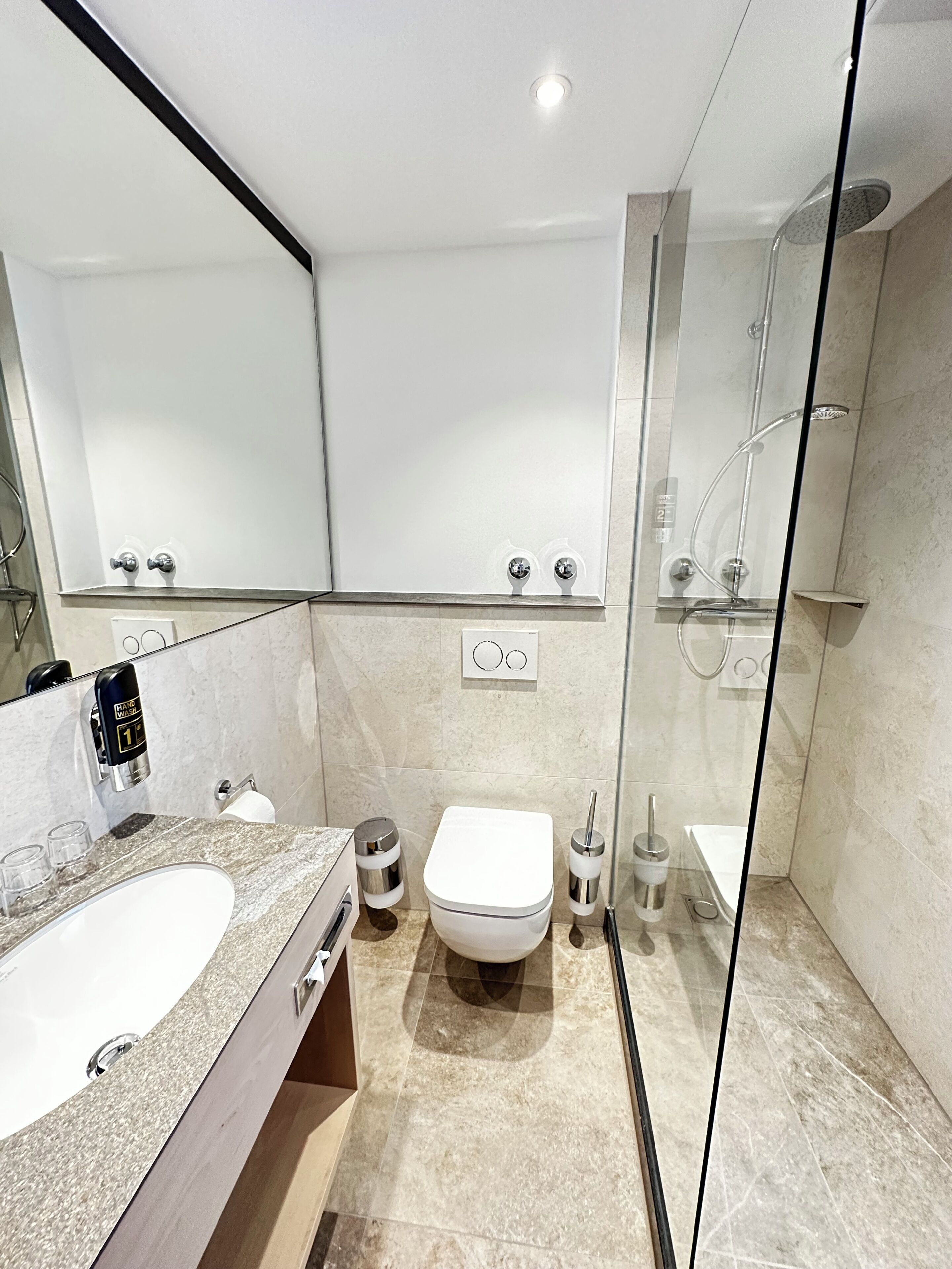 Un baño moderno con ducha envuelta en vidrio, inodoro blanco y lavamanos con encimera de granito.
