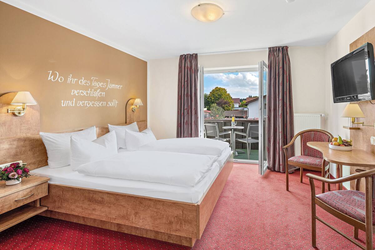 A hotel room with a bed, a desk, a chair, a TV, and a balcony with curtains.