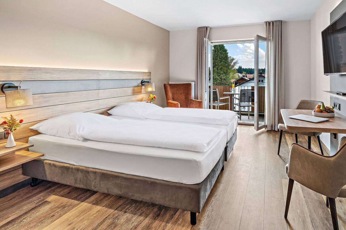 A hotel room with a large bed, a desk with a chair, a TV, and a balcony with a view of the outside.