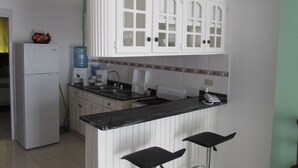 Une cuisine avec des meubles blancs, un réfrigérateur, un distributeur d’eau, une machine à café et une cuisinière à gaz.