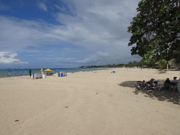 Ein Strand mit Sonnenschirmen, Liegestühlen und entspannten Personen.