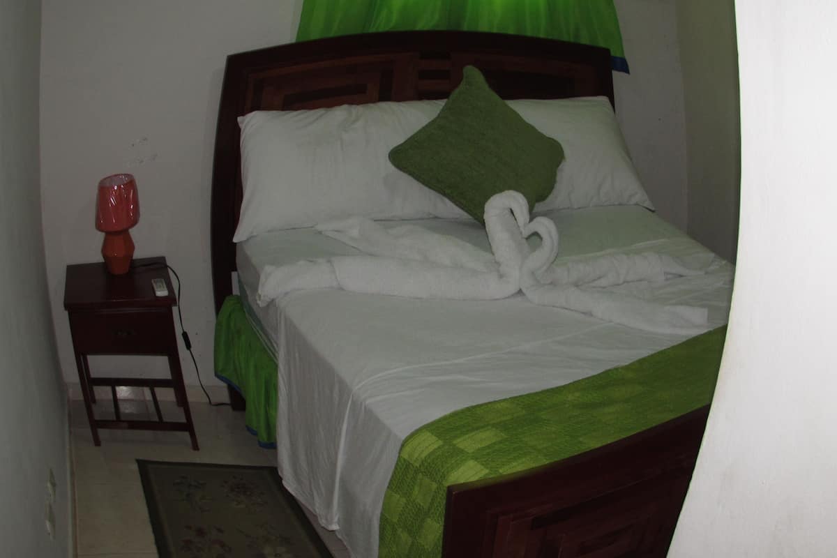A neatly made bed with a green bedspread and a white pillow.