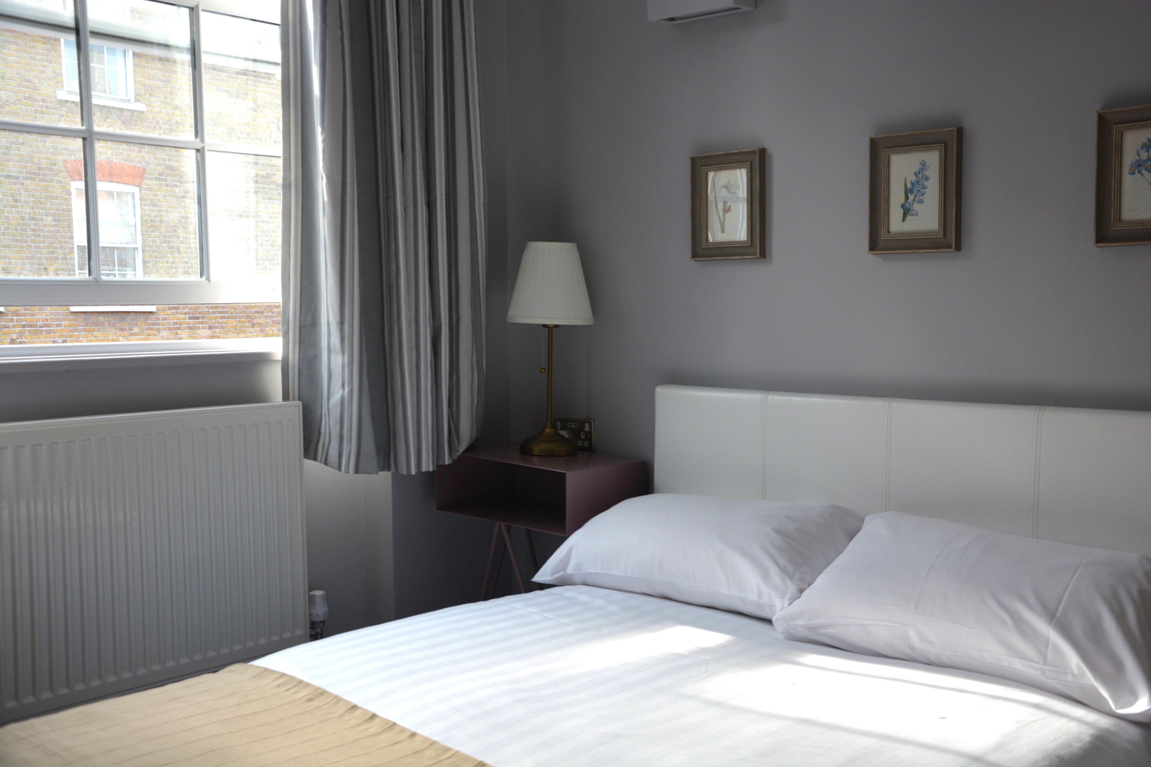 A hotel room with a bed, a nightstand, a lamp, and two framed pictures on the wall.