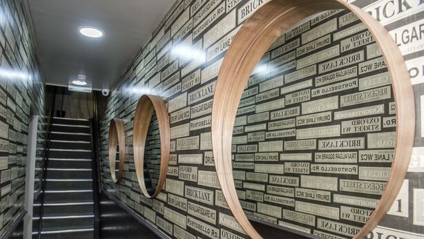 A hallway with a brick-patterned wall and circular wooden structures. - Monopoly Accommodations (London)