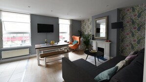 A modern living room with a sofa, a chair, a dining table, and a fireplace. - Monopoly Accommodations (London)