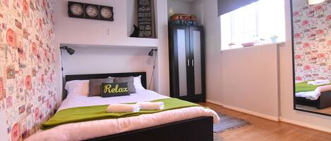 Un dormitorio con cama, armario, espejo y una pared con relojes.