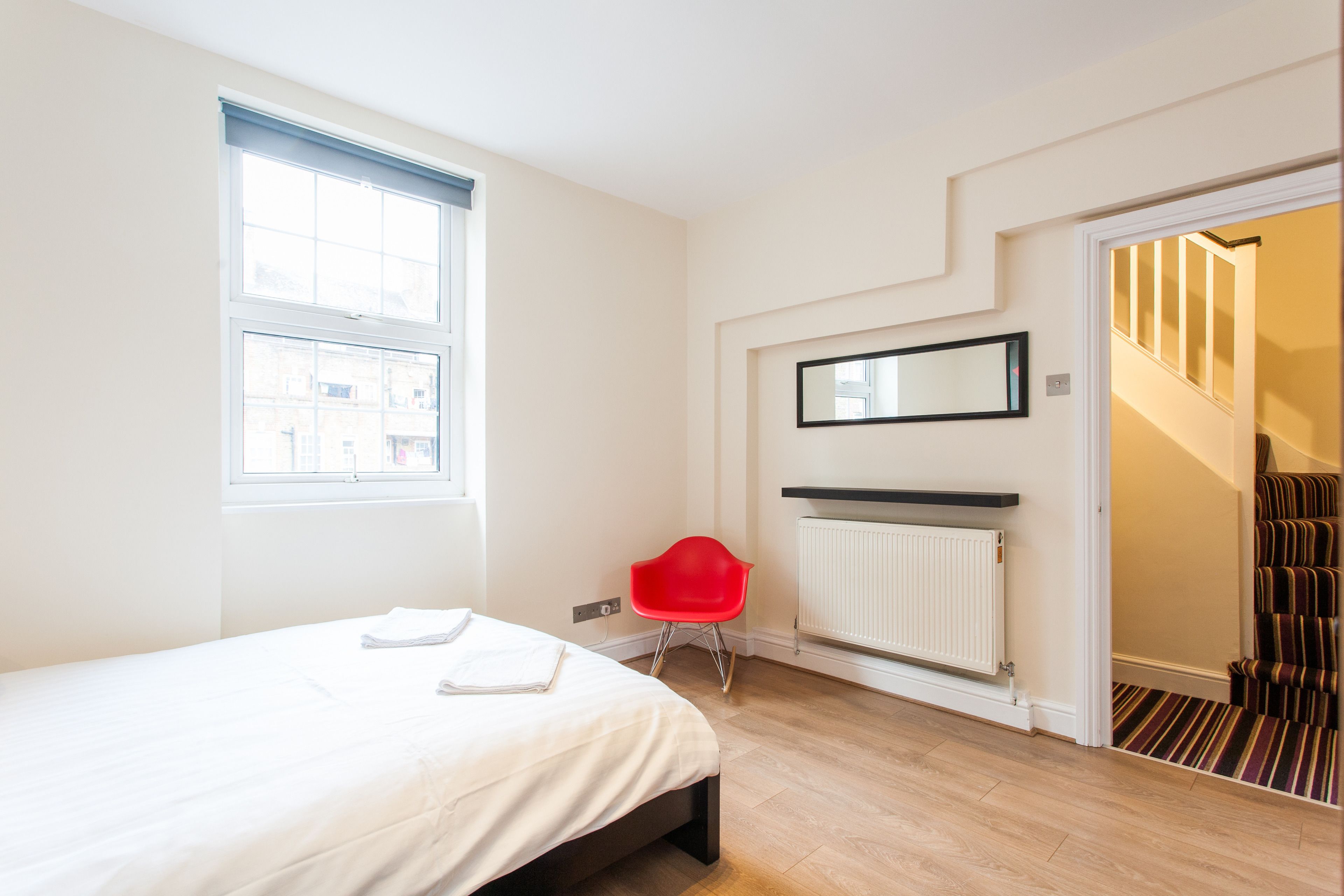 Une chambre moderne avec un lit, un fauteuil rouge, un radiateur et un escalier menant à une autre pièce.