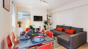 A modern living room with a grey sofa, red chairs, and a dining table set for four. - Monopoly Accommodations (London)