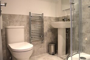 A modern bathroom with a toilet, a sink, a glass-enclosed shower, and a trash bin.