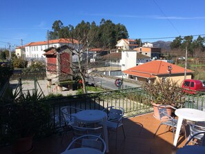 A terrace with outdoor seating, a view of residential buildings, and a red vehicle parked on the street. - Hostel do Ermal (Vieira do Minho)