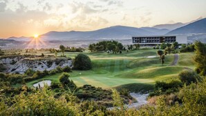 Ein modernes Gebäude mit flachem Dach und großen Fenstern, umgeben von einem gepflegten Golfplatz mit Sandbunkern und Bäumen.