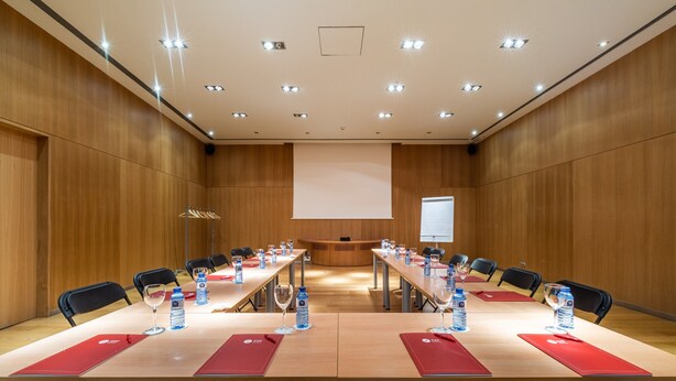A conference room with long tables, chairs, water bottles, and red placemats. - Exe Las Margas Golf (Sabinanigo)