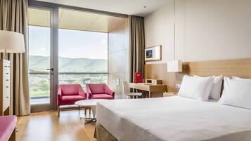 A hotel room with a large bed, a desk, a chair, and a view of the outdoors.
