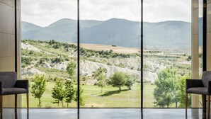 Ein Zimmer mit großem Fenster und Blick auf eine gebirgige Landschaft. Vor dem Fenster stehen zwei Stühle.