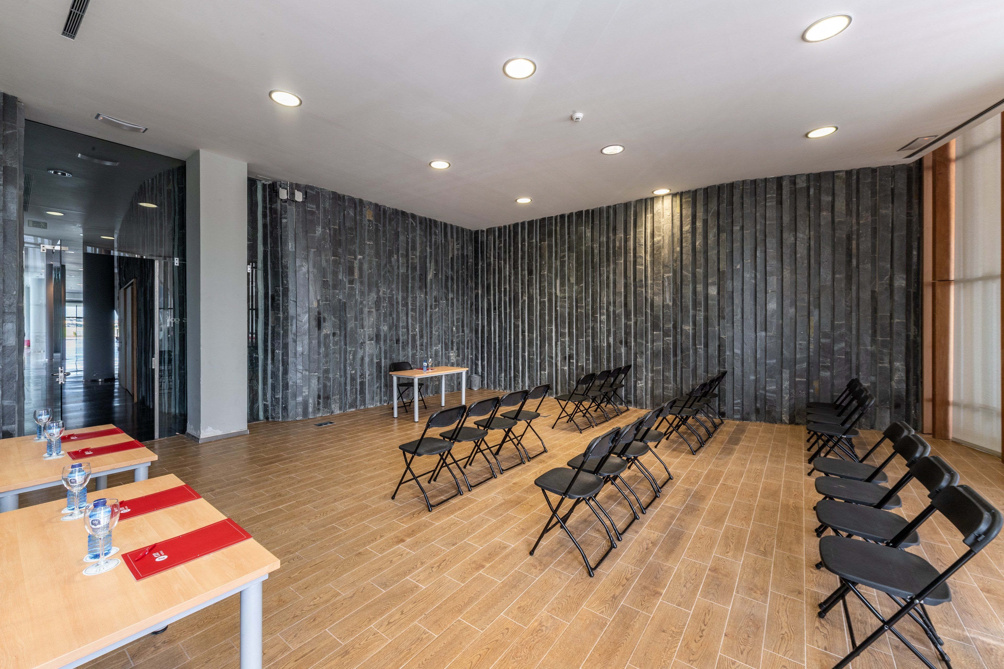 A conference room with foldable chairs, a table with water glasses, and a dark marble wall.