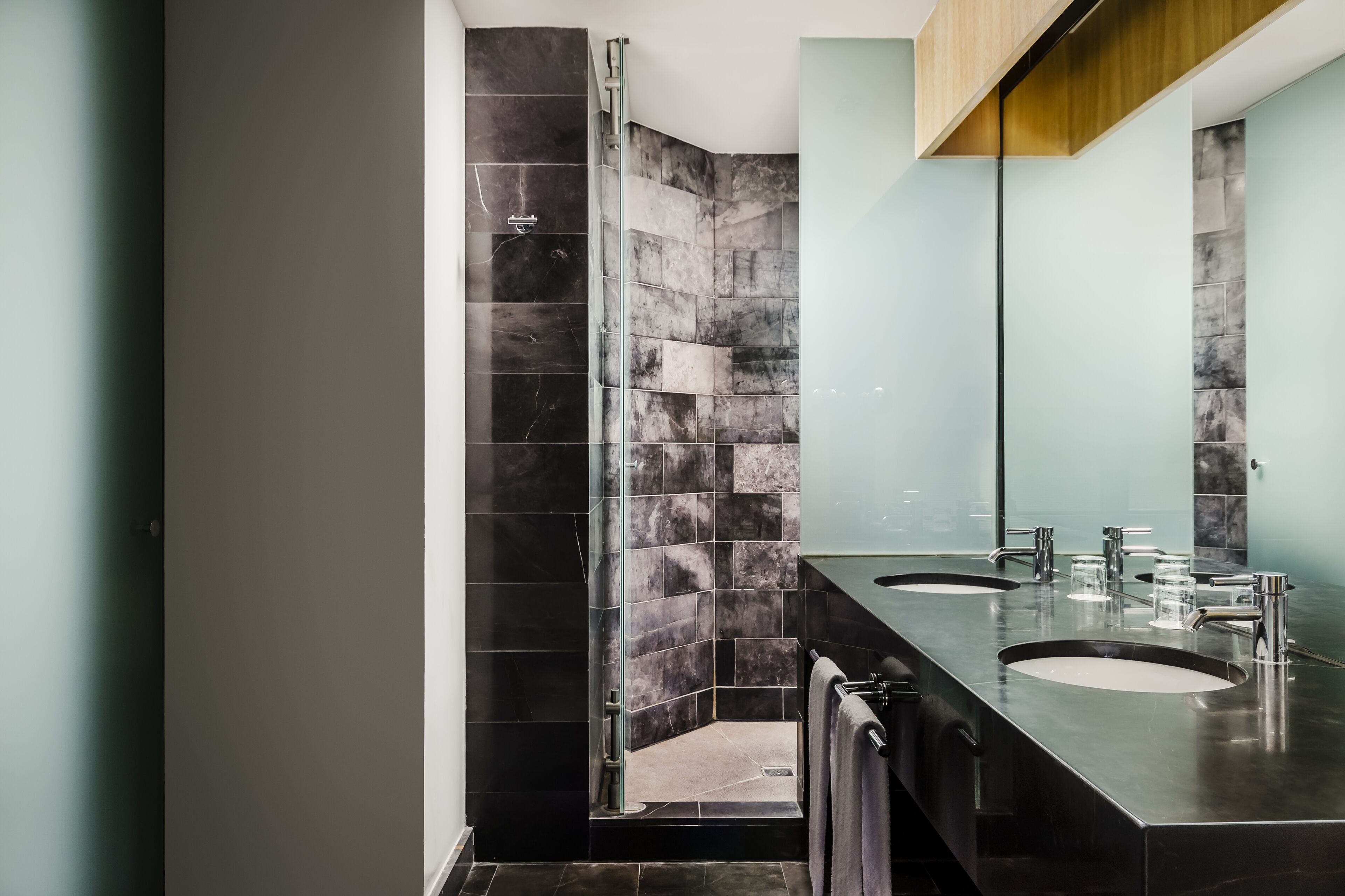 Un baño moderno con ducha de vidrio, dos lavamanos y un espejo grande.